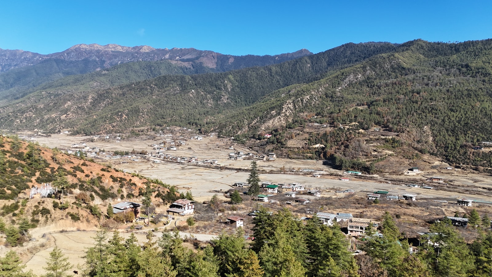 Scattered village houses across a broad rural Bhutanese valley